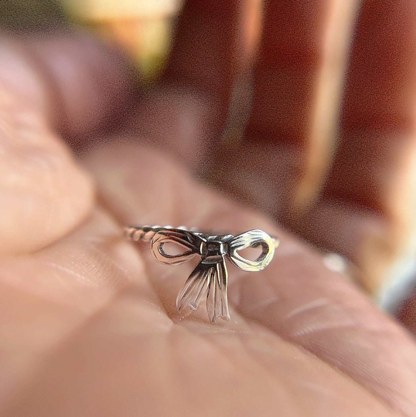 Silver bow ring sitting on a hand with blurred background