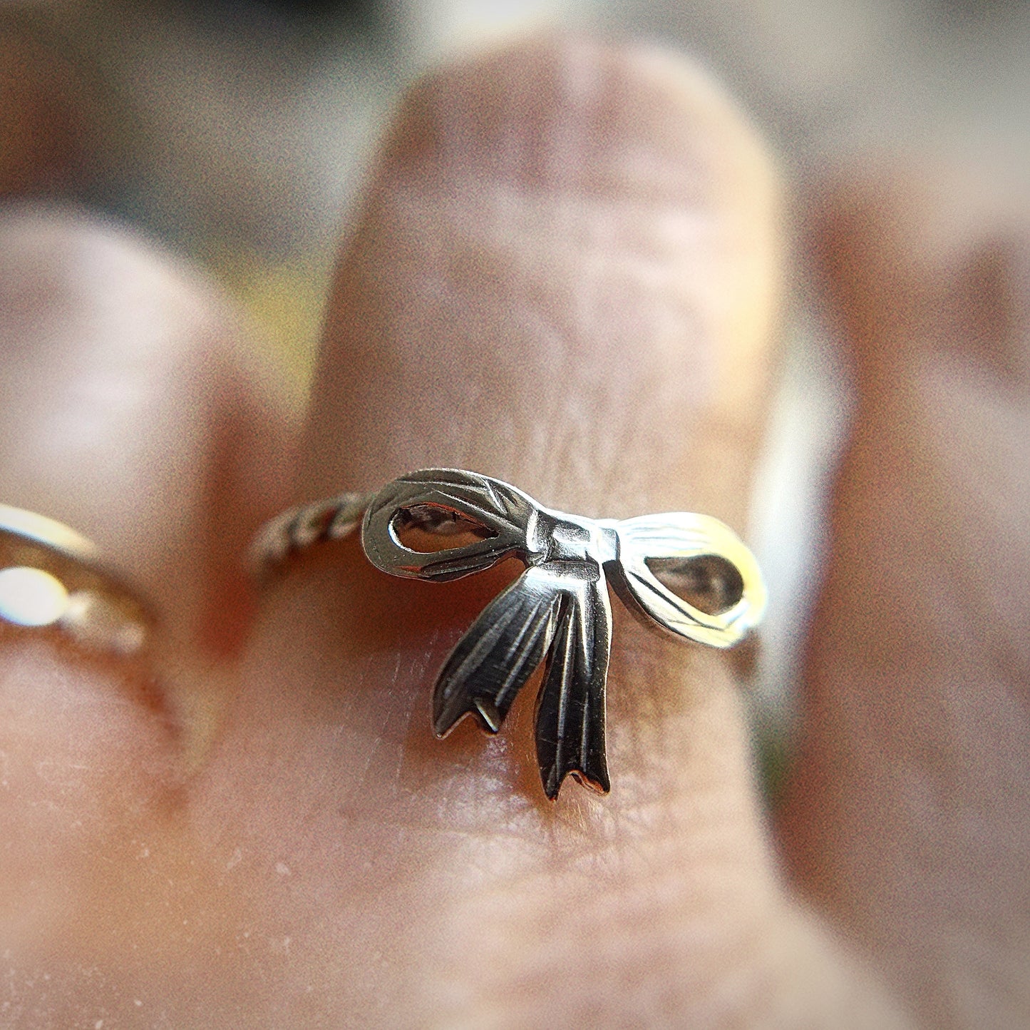 Silver bow ring on blurred white hand with a dreamy filter
