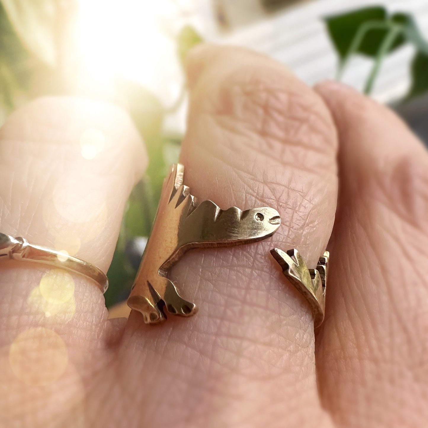 gold stegosaurus dino ring on woman's hand. the ring wraps around with the head and the tail meeting in the front. 