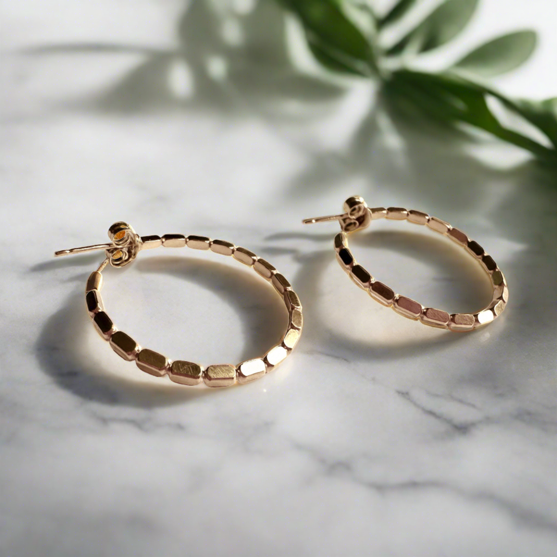 gold beaded hoop earrings with marble and foliage background