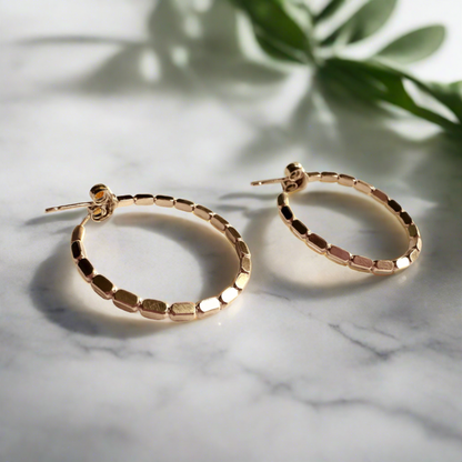 gold beaded hoop earrings with marble and foliage background