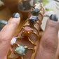 raw gemstone rings containing ametrine, emerald, sapphire, sunstone and labradorite on a woman's hand with forest green fingernail polish
